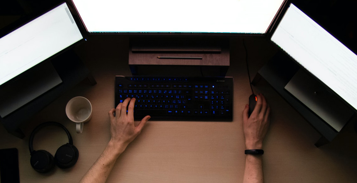 A person working at a desk with 3 monitors