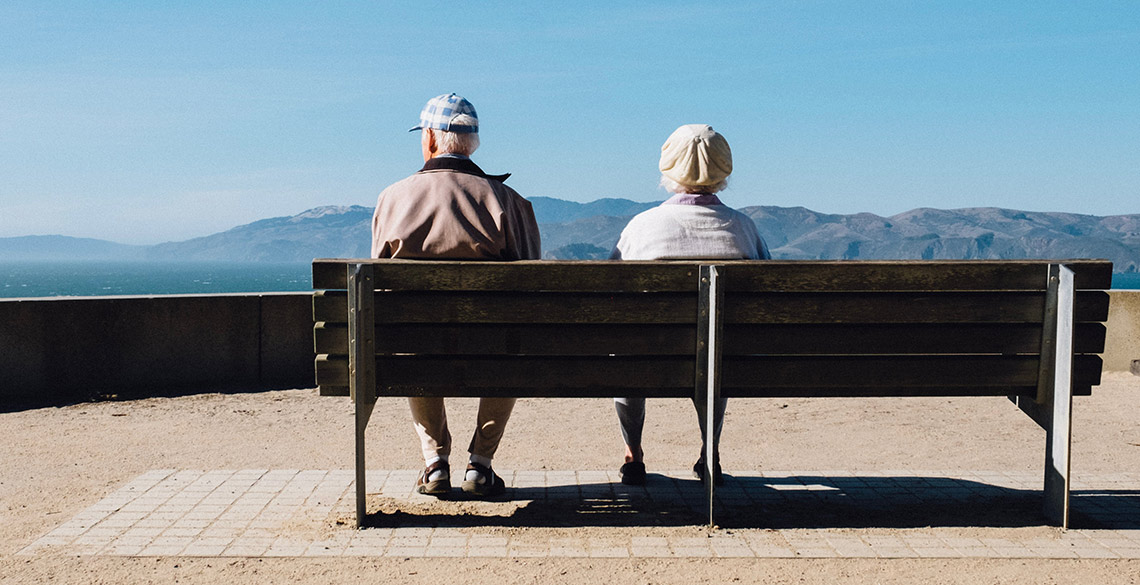 Elderly couple sitting on a bench looking out to sea