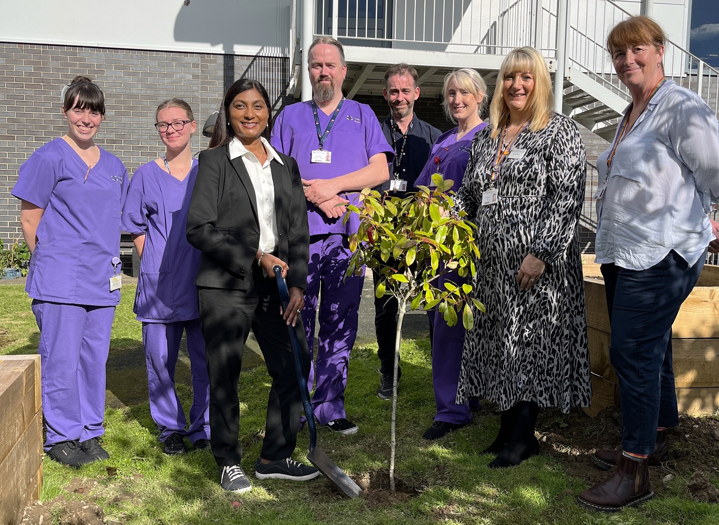 Chief Nursing Officer Sue Tranka and Amanda Jones, Principal in Healthcare Education at Aberystwyth University, with other staff and students planting the tree to mark the start of the new wellbeing garden