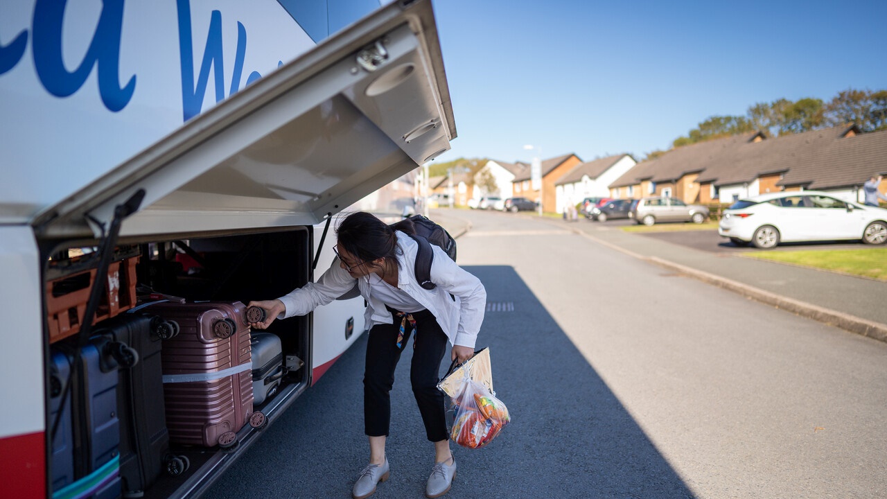 Student putting luggage on bus